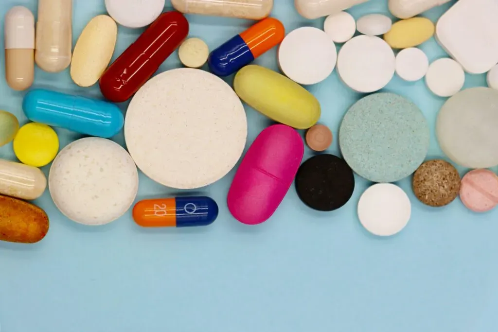 Różnokolorowe tabletki i kapsułki na jasnoniebieskim tle – ilustracja do sekcji prawo farmaceutyczne i weterynaryjne kancelarii KRK