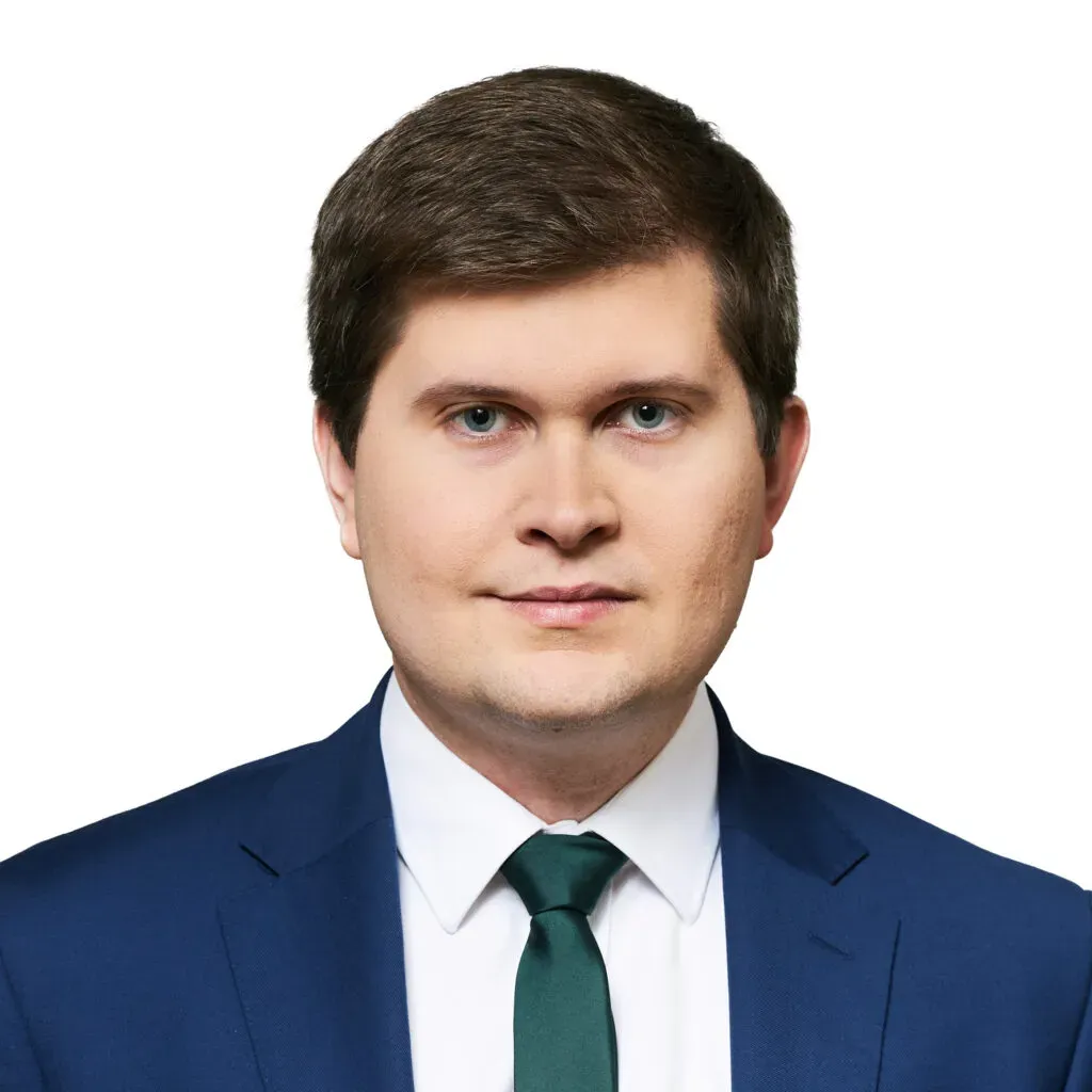 Adwokat kancelarii KRK z krótkimi ciemnobrązowymi włosami, w granatowym garniturze, białej koszuli i zielonym krawacie – zdjęcie biznesowe do sekcji Zespół