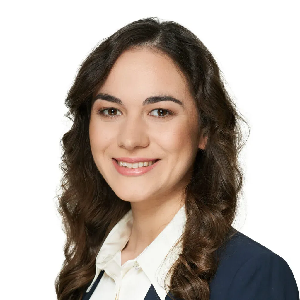 Aplikantka adwokacka kancelarii KRK z długimi, ciemnymi, falowanymi włosami, w granatowym żakiecie i kremowej koszuli – zdjęcie biznesowe do sekcji Zespół