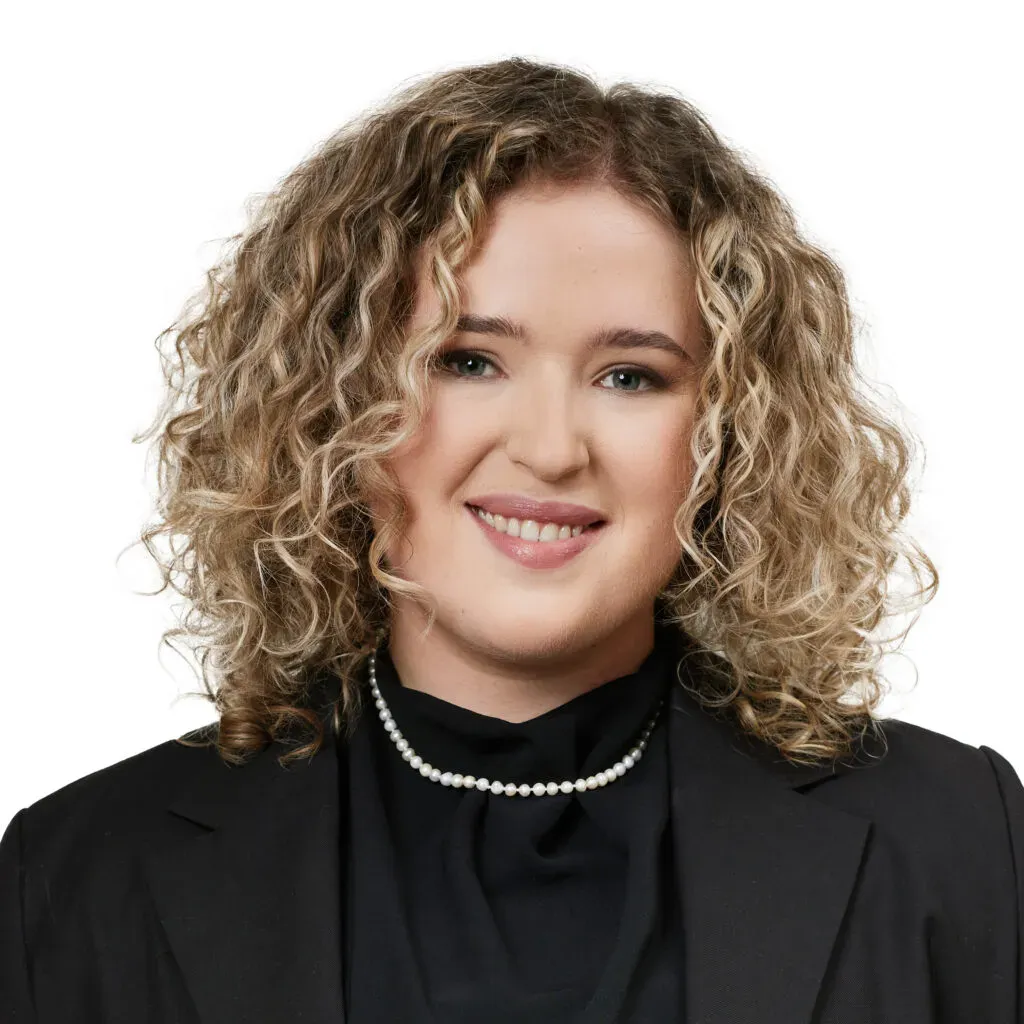 Aplikantka adwokacka kancelarii KRK z jasnymi kręconymi włosami, w czarnym żakiecie i eleganckiej bluzce z perłowym naszyjnikiem – profesjonalny portret do sekcji Zespół