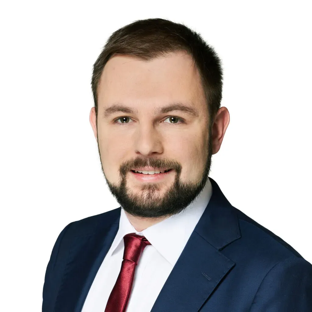 Adwokat kancelarii KRK z krótkimi brązowymi włosami i brodą, w granatowym garniturze, białej koszuli i bordowym krawacie – profesjonalny portret do sekcji Zespół