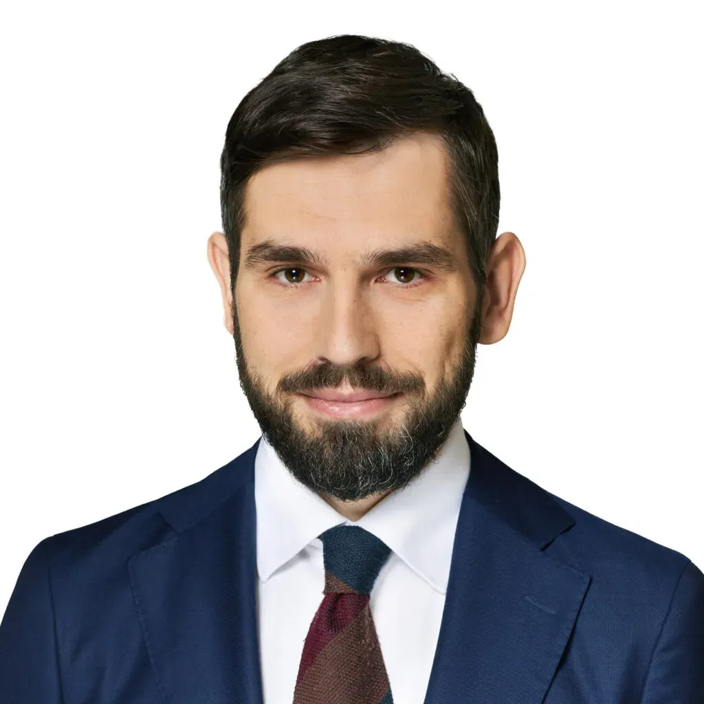 Partner, adwokat kancelarii KRK z krótkimi ciemnymi włosami i brodą, w granatowym garniturze, białej koszuli i krawacie w odcieniach bordo – profesjonalny portret do sekcji Zespół