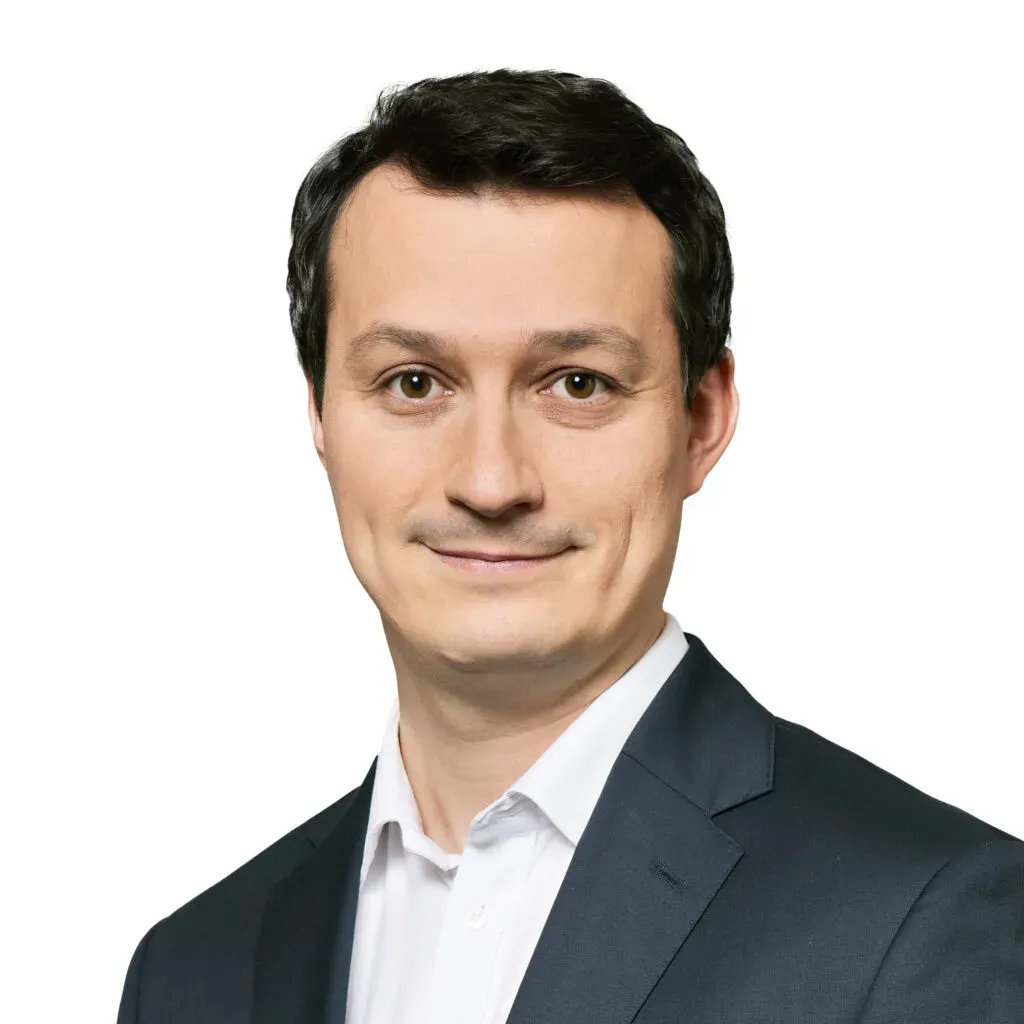 Partner, radca prawny kancelarii KRK z krótkimi ciemnobrązowymi włosami, w granatowym garniturze i białej koszuli – profesjonalny portret do sekcji Zespół