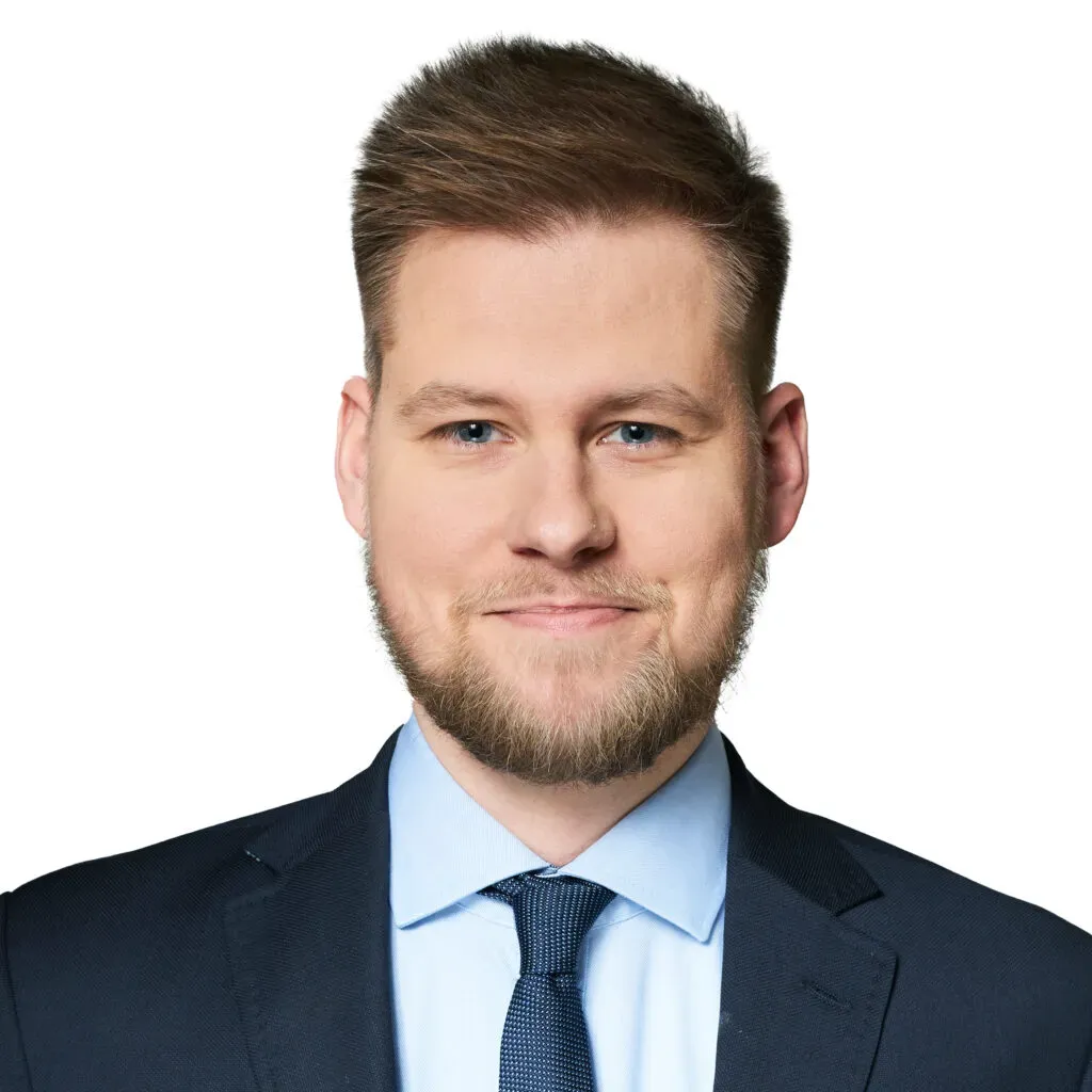 Aplikant radcowski kancelarii KRK z krótkimi jasnobrązowymi włosami i brodą, w granatowym garniturze i błękitnej koszuli – profesjonalny portret do sekcji Zespół