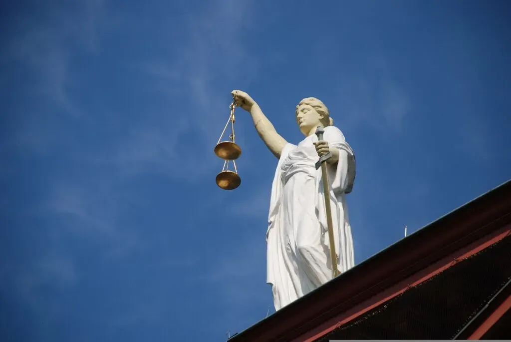 Posąg Temidy trzymającej wagę i miecz na tle nieba – ilustracja do sekcji spory sądowe i arbitraż w kancelarii KRK