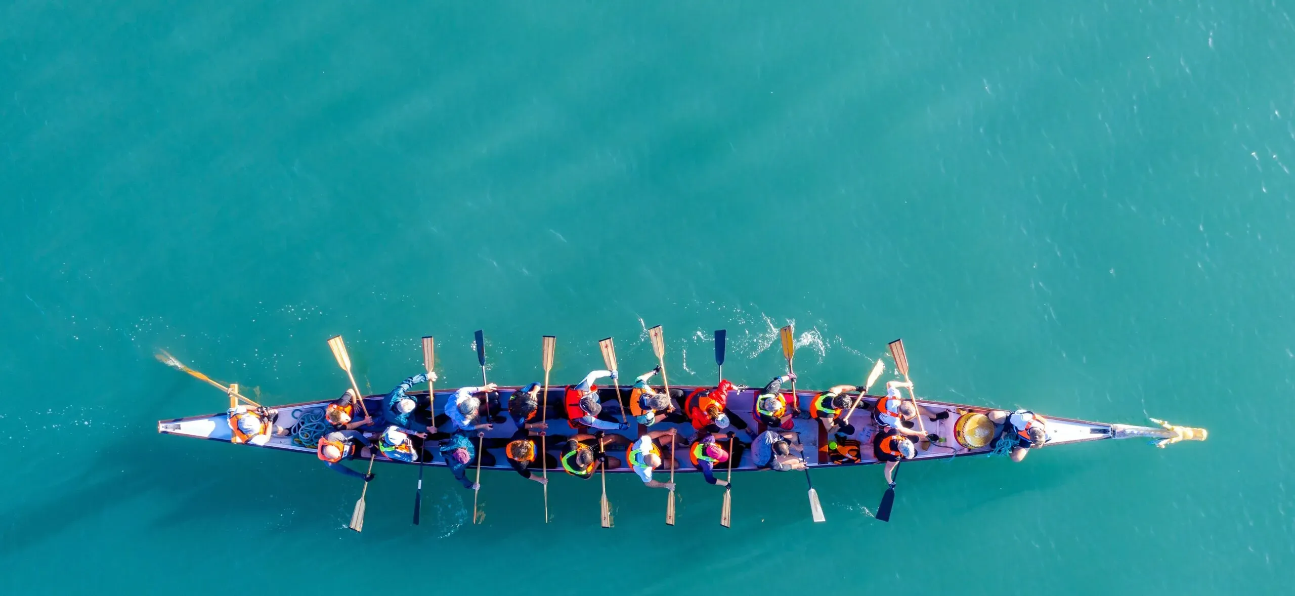 Zespół ludzi wiosłujący wspólnie w łodzi na wodzie – metaforyczna ilustracja współpracy i pracy zespołowej w kancelarii KRK.”