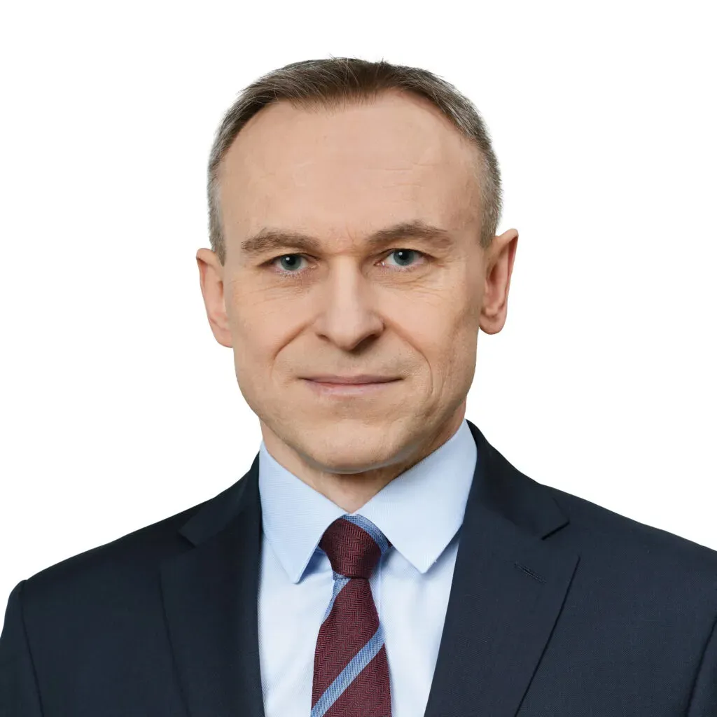 Wspólnik, radca prawny kancelarii KRK z krótkimi jasnobrązowymi włosami, w granatowym garniturze, błękitnej koszuli i bordowo-niebieskim krawacie – profesjonalny portret do sekcji Zespół